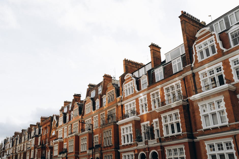 Exterior view of a row of multi-story residential buildings in West Hampstead, showing a mix of brick and white-painted facades. The white section features large windows, a small balcony with green pl