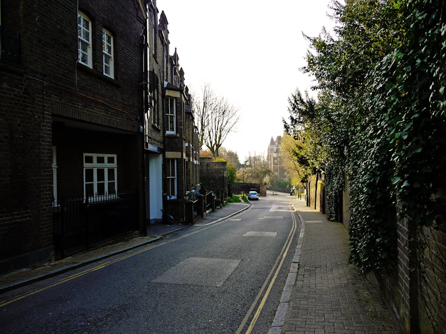 A narrow, cobblestone street in West Hampstead lined with residential buildings made of dark brick and painted white façades. The street is clean and well-maintained, with a small lamppost on the sid